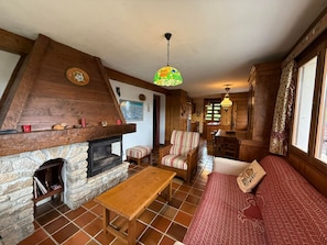 Ein gemütliches Wohnzimmer mit Kamin aus Stein, Holzmöbeln und einer farbenfrohen Hängelampe.