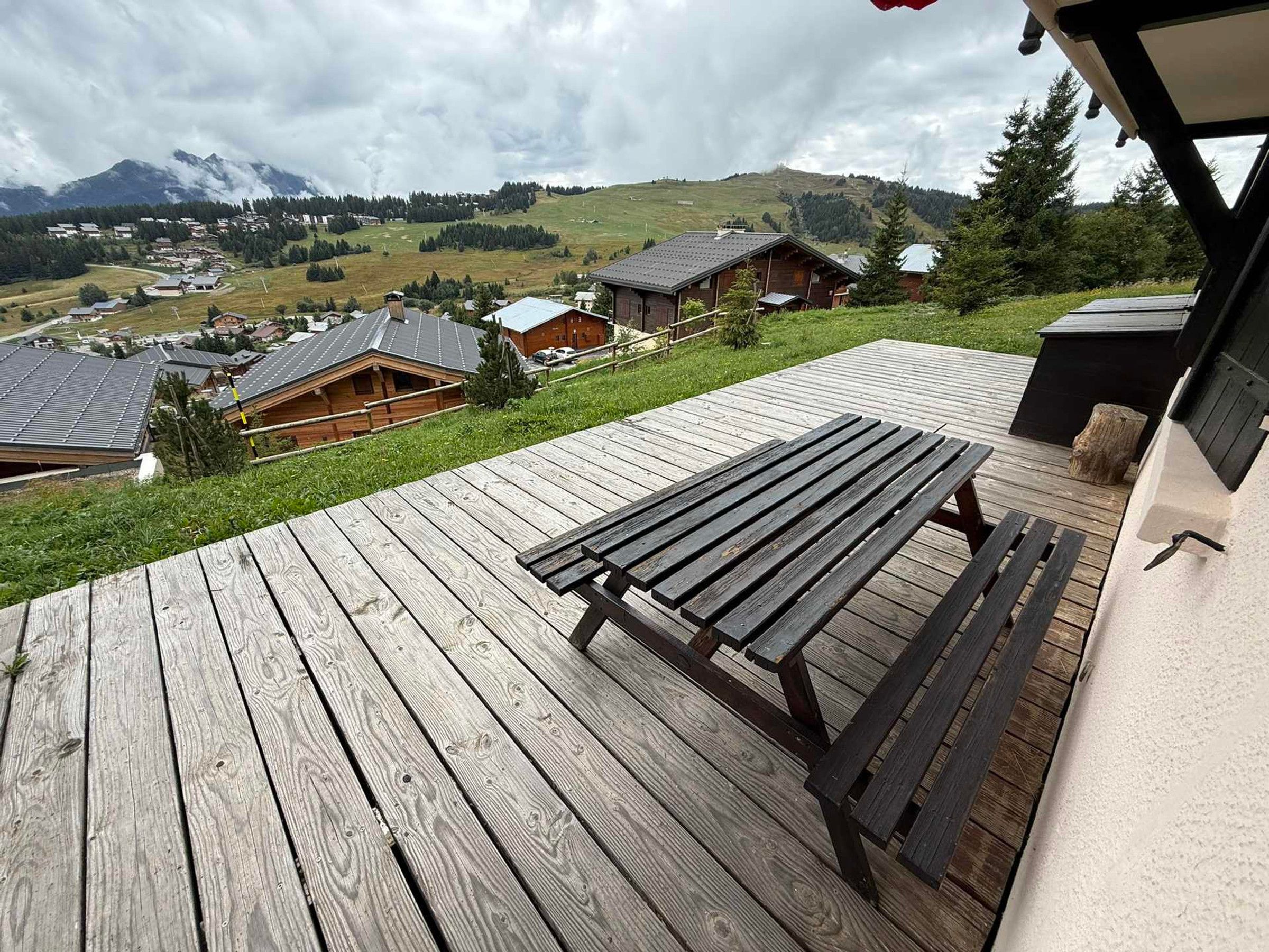 Eine Holzterrasse mit einer Bank, mit Blick auf ein Dorf, Häuser und Berge im Hintergrund.