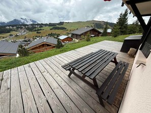Un terrazzo in legno con una panchina, affacciato su un villaggio con case e montagne sullo sfondo.