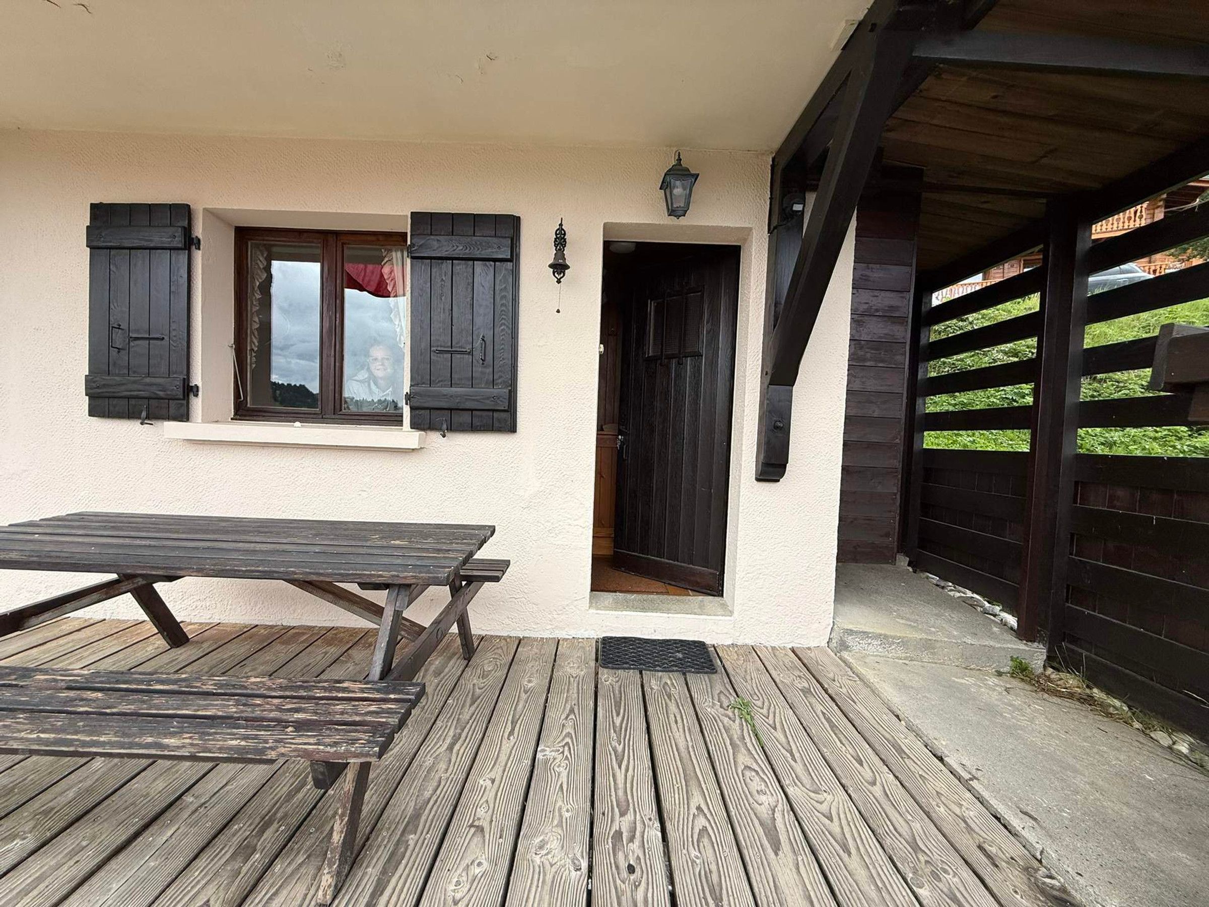 A wooden deck with a picnic table, a building with a white exterior, and a dark wooden gate.