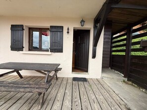 A wooden deck with a picnic table, a building with a white exterior, and a dark wooden gate. - Cozy and quiet apartment - 6 guests (Les Saisies)