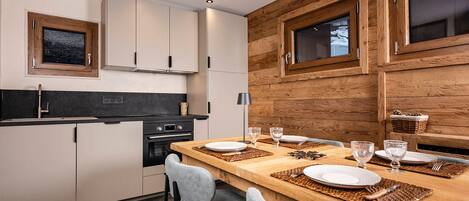 Une cuisine moderne avec un mur d’accent en bois, des placards intégrés et un coin repas aménagé pour quatre personnes.