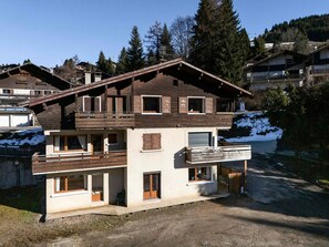 Eine mehrstöckige Holzhütte mit Balkon, Garage und Blick auf eine verschneite Landschaft.