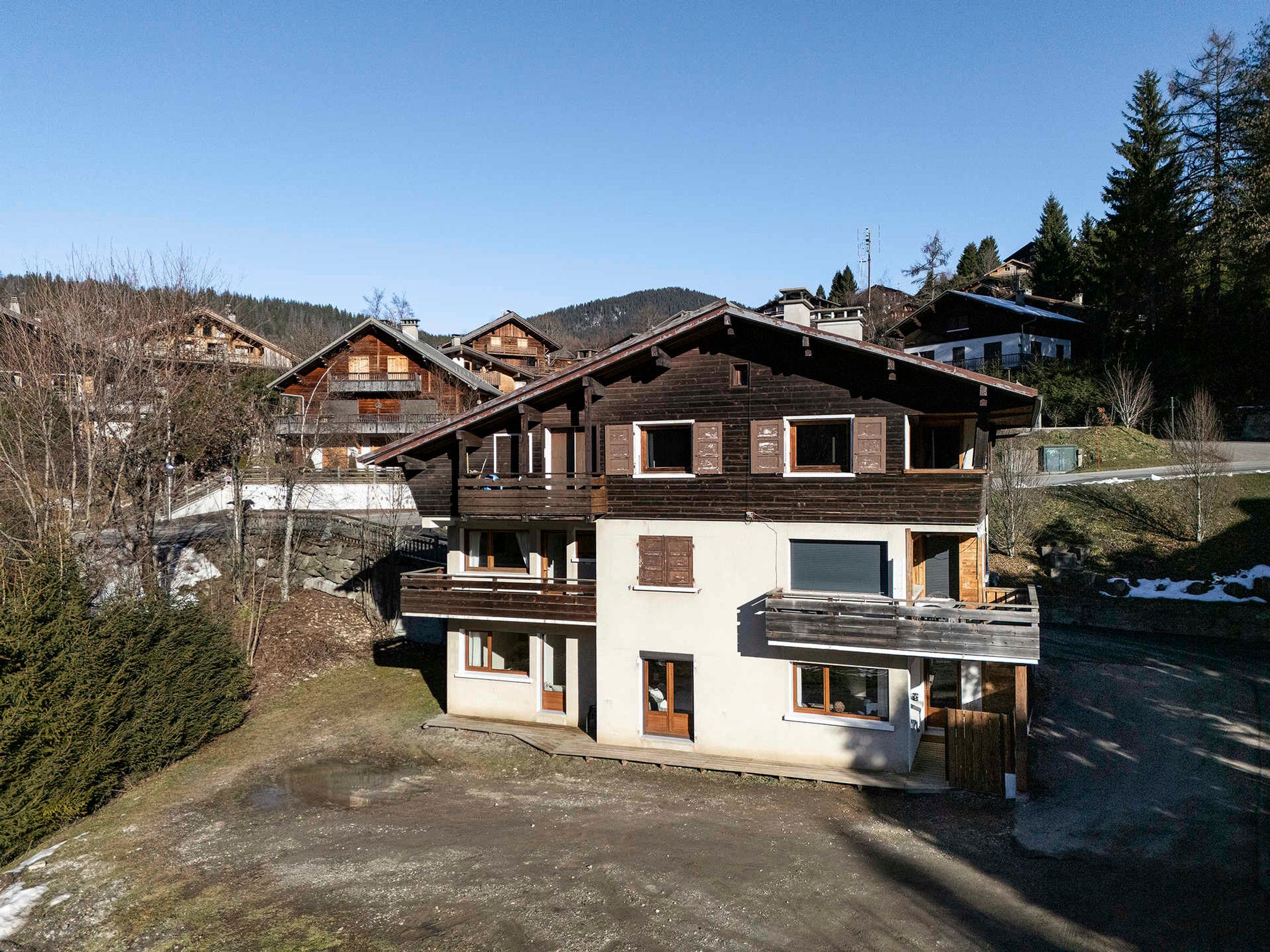 Un chalet à plusieurs étages, doté d’une façade en bois, de balcons et d’une piste de ski en arrière-plan.