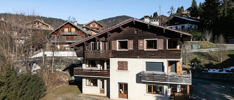 A multi-story chalet with a wooden facade, balconies, and a ski slope in the background.