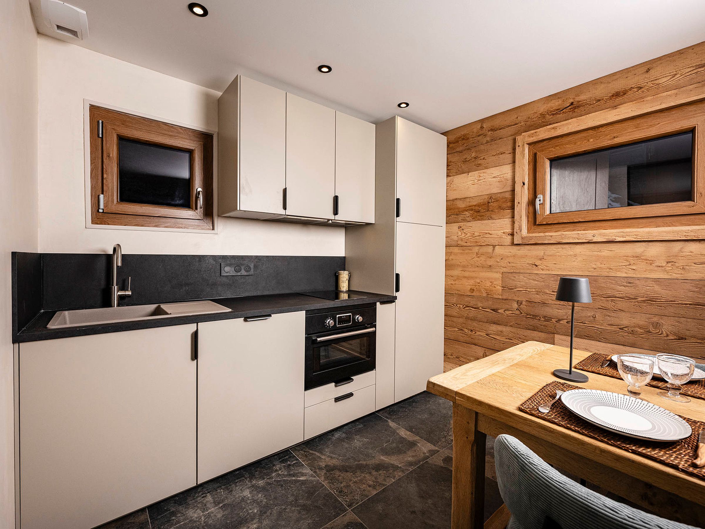 Cocina compacta con armarios blancos, encimera negra y panel de pared de madera.