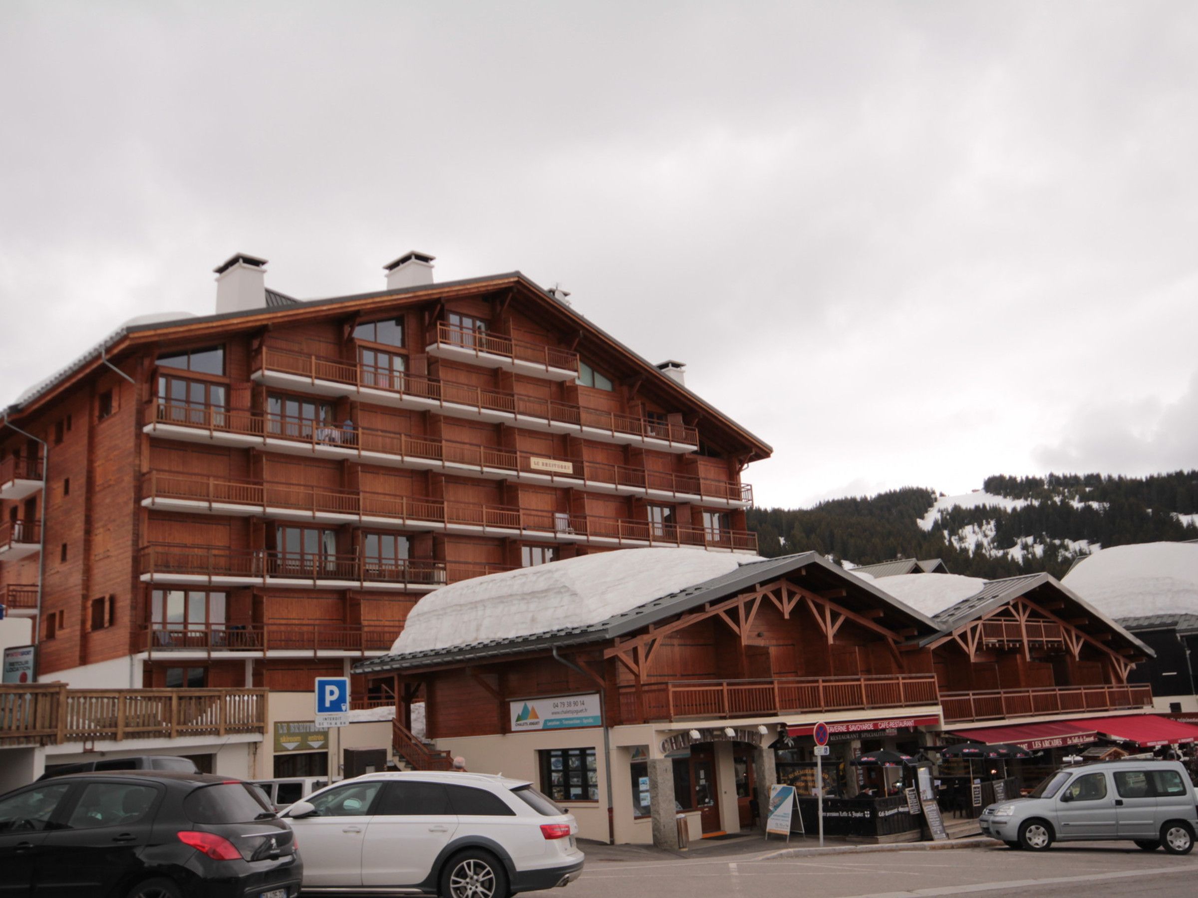 A multi-story wooden building with balconies, a parking sign, and a restaurant with outdoor seating.