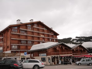A multi-story wooden building with balconies, a parking sign, and a restaurant with outdoor seating. - Spacious apartment slope views - 8 guests (Les Saisies)