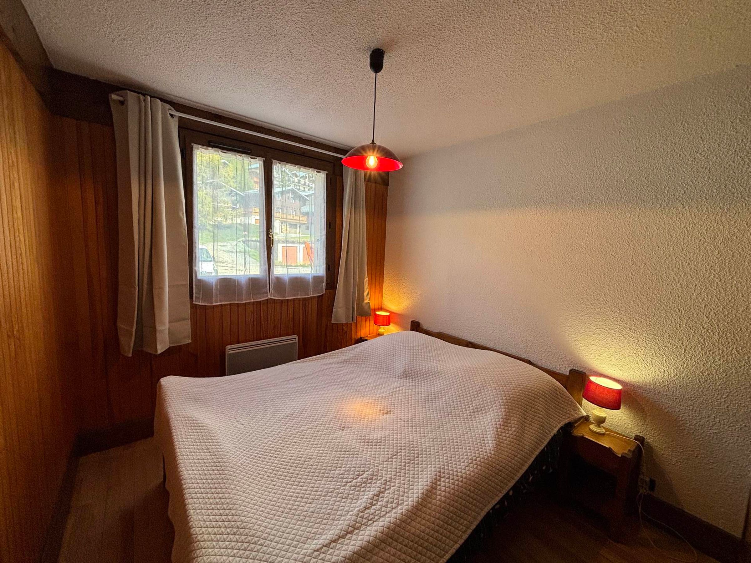 Un dormitorio con cama, una ventana con cortinas, una lámpara de pared y un radiador.