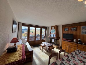 Un salon chaleureux avec un canapé, une table recouverte d’une courtepointe, une cheminée et un téléviseur.