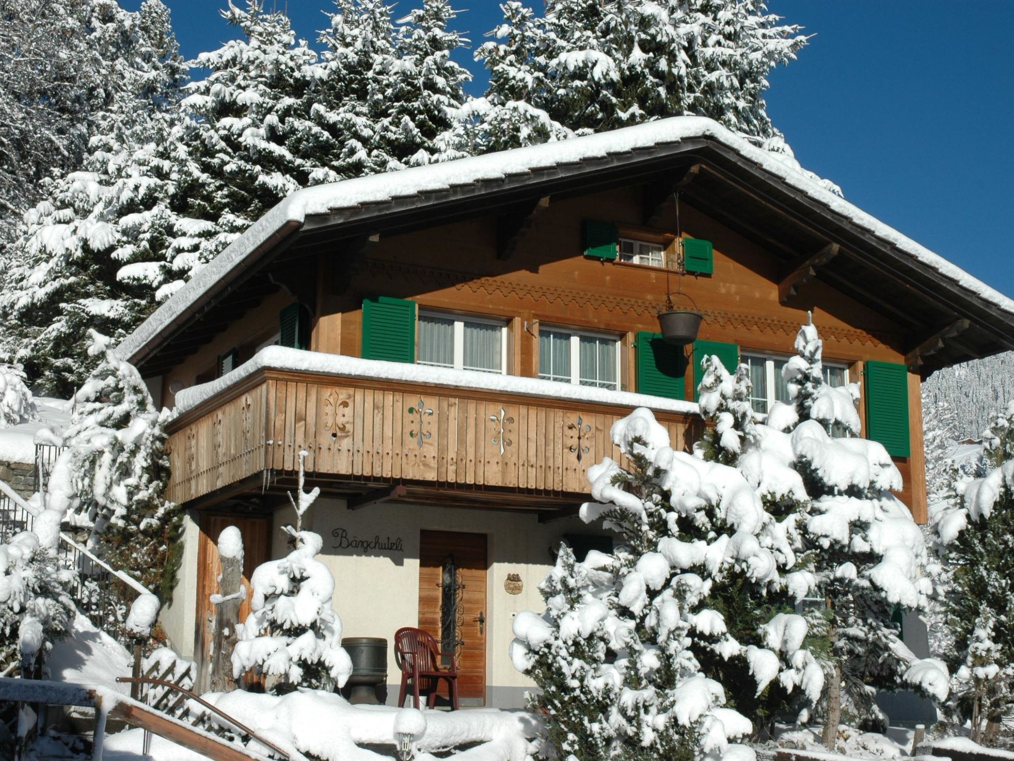Un chalet en bois doté d’un balcon, entouré d’arbres couverts de neige.