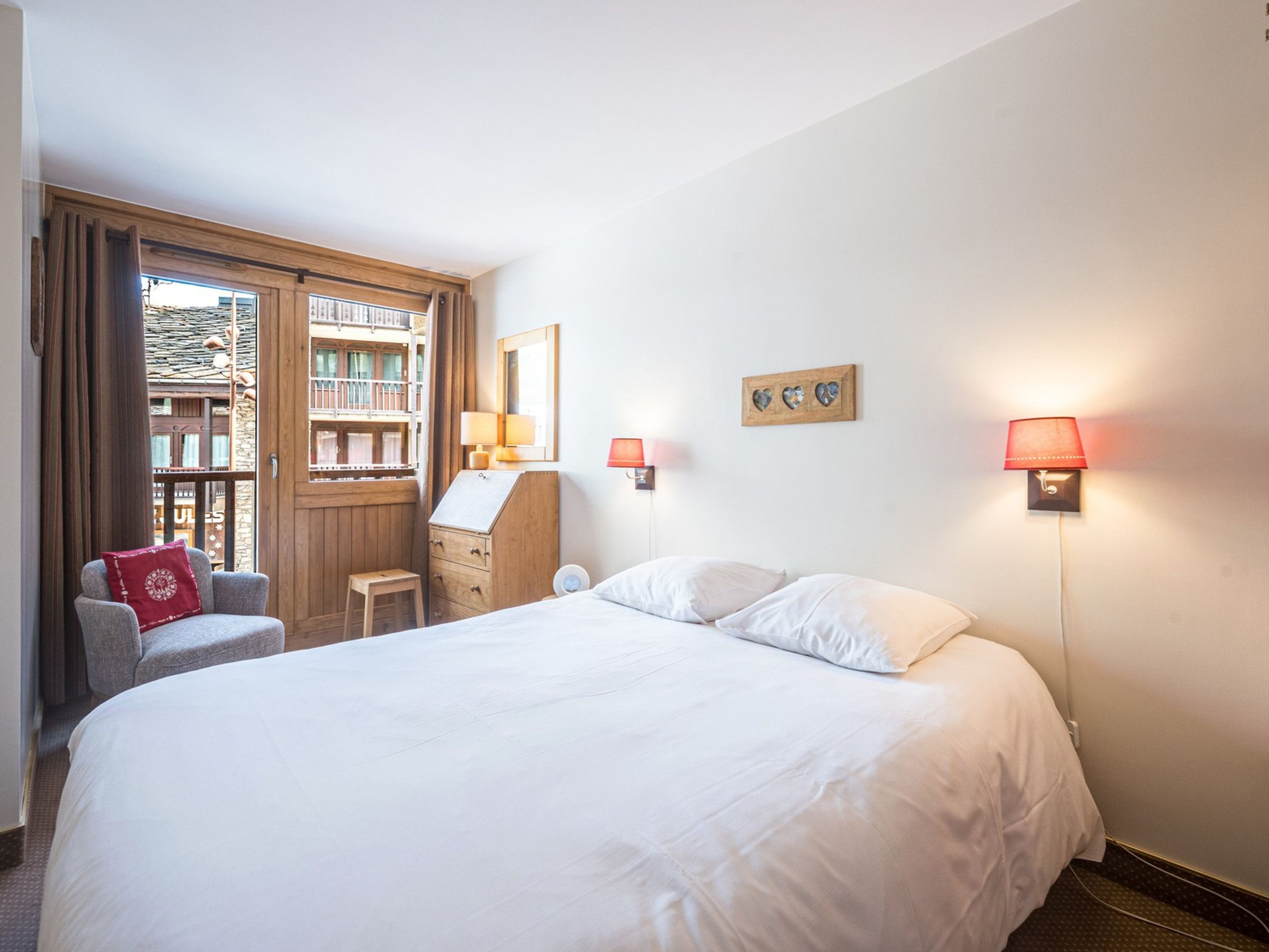 Une chambre d’hôtel avec un grand lit, un bureau avec une chaise, une fenêtre donnant sur des immeubles et deux lampes fixées au mur.