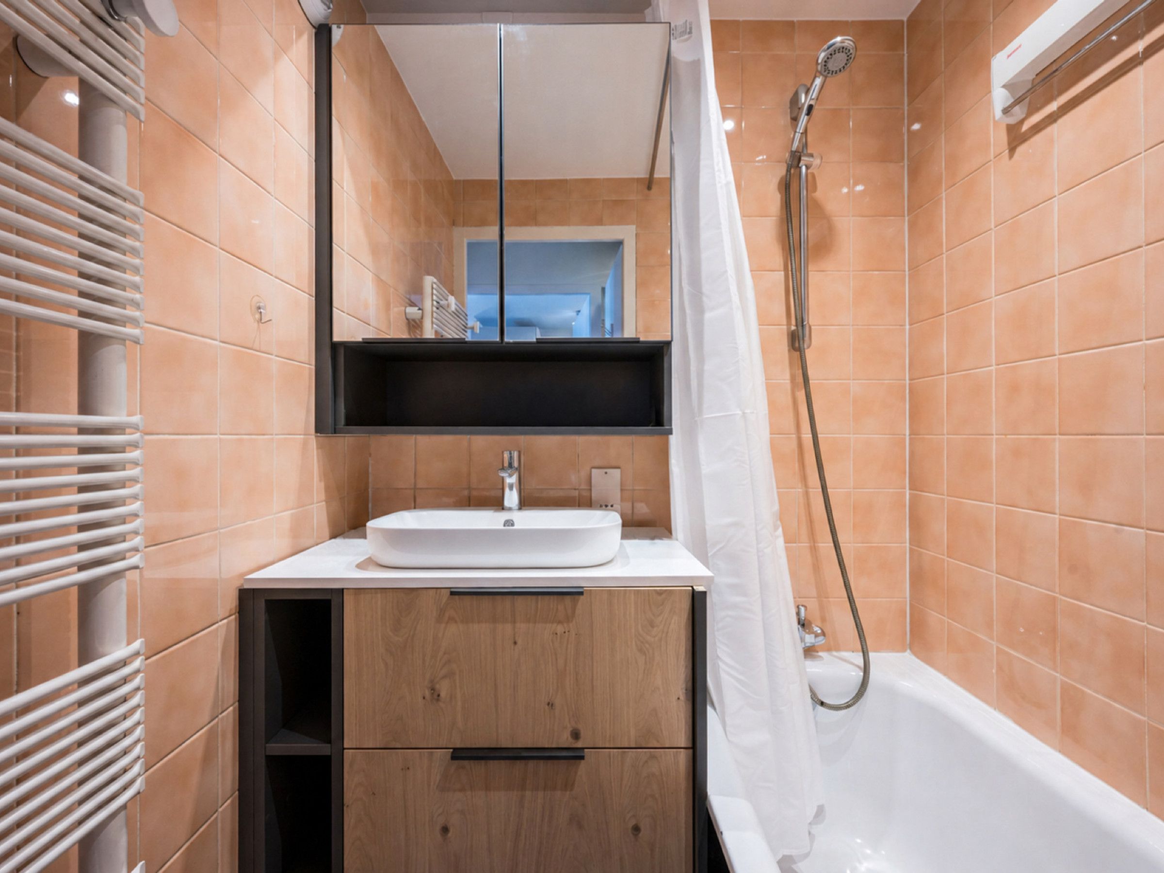 A modern bathroom with a white sink, wooden cabinet, and a shower with a curtain.