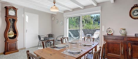 Un comedor con una mesa de madera dispuesta para cuatro, rodeada de sillas, un aparador de madera grande y un reloj fijado a la pared.