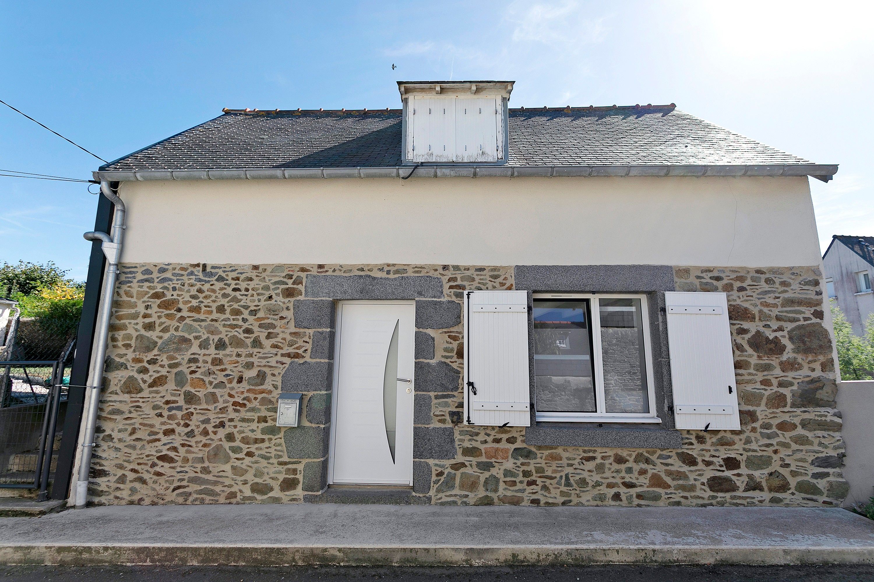 Edificio de fachada de piedra con dos ventanas enmarcadas en blanco y un pequeño ventanuera.