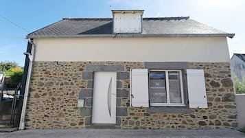 Edificio de fachada de piedra con dos ventanas enmarcadas en blanco y un pequeño ventanuera.