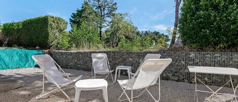 Un espace extérieur aménagé avec des chaises et des tables blanches, entouré d’un sol en gravier et d’un mur en pierre.