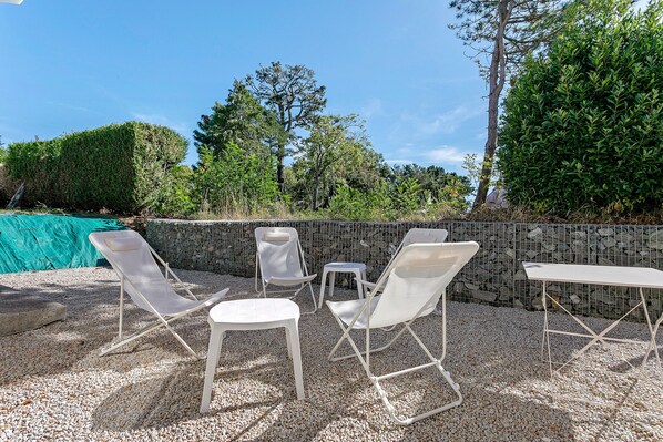 An outdoor seating area with white chairs and tables, surrounded by a gravel ground and a stone wall.