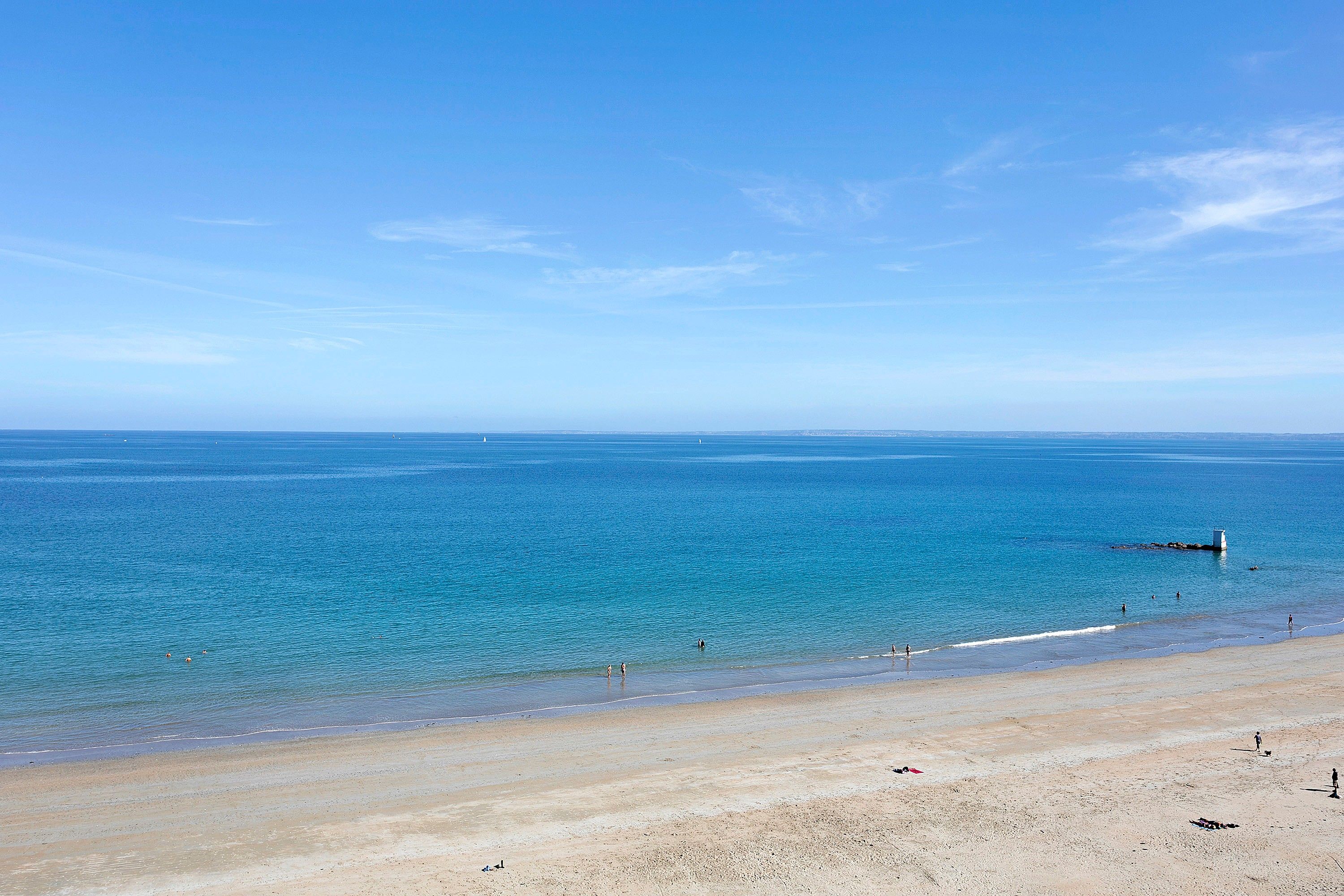 Une plage avec une eau d’un bleu limpide et un rivage sablonneux.