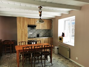 Ett kök med träskåp, en mönstrad väggbeklädnad bakom arbetsbänken, ett matbord med stolar och ett fönster med utsikt.