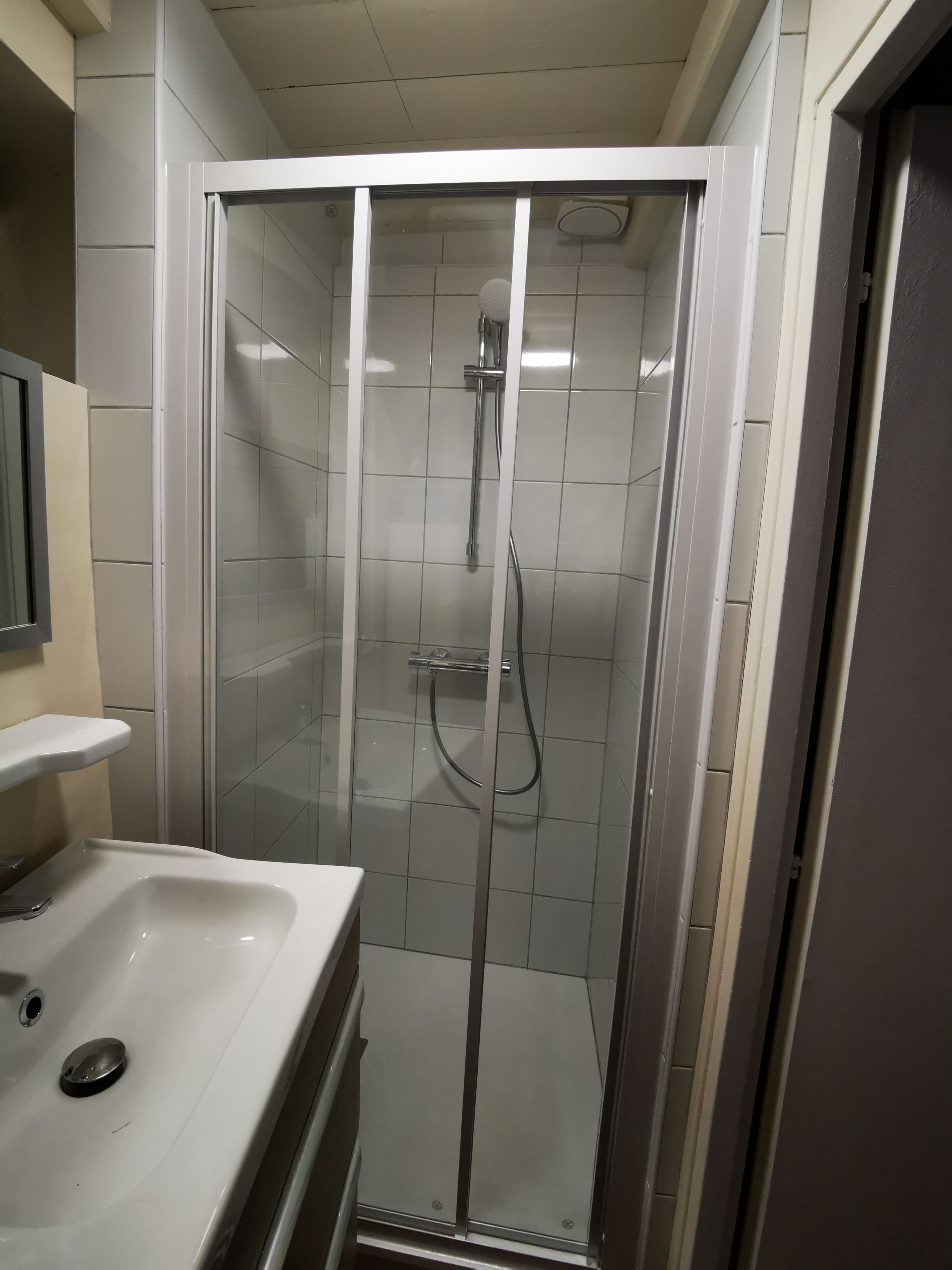 Ett badrum med en dusch som är avskärmad med glasväggar, ett vitt handfat och en spegel.