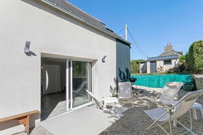 Un patio con mesa y sillas, una puerta corrediza de vidrio y vista a una casa vecina.
