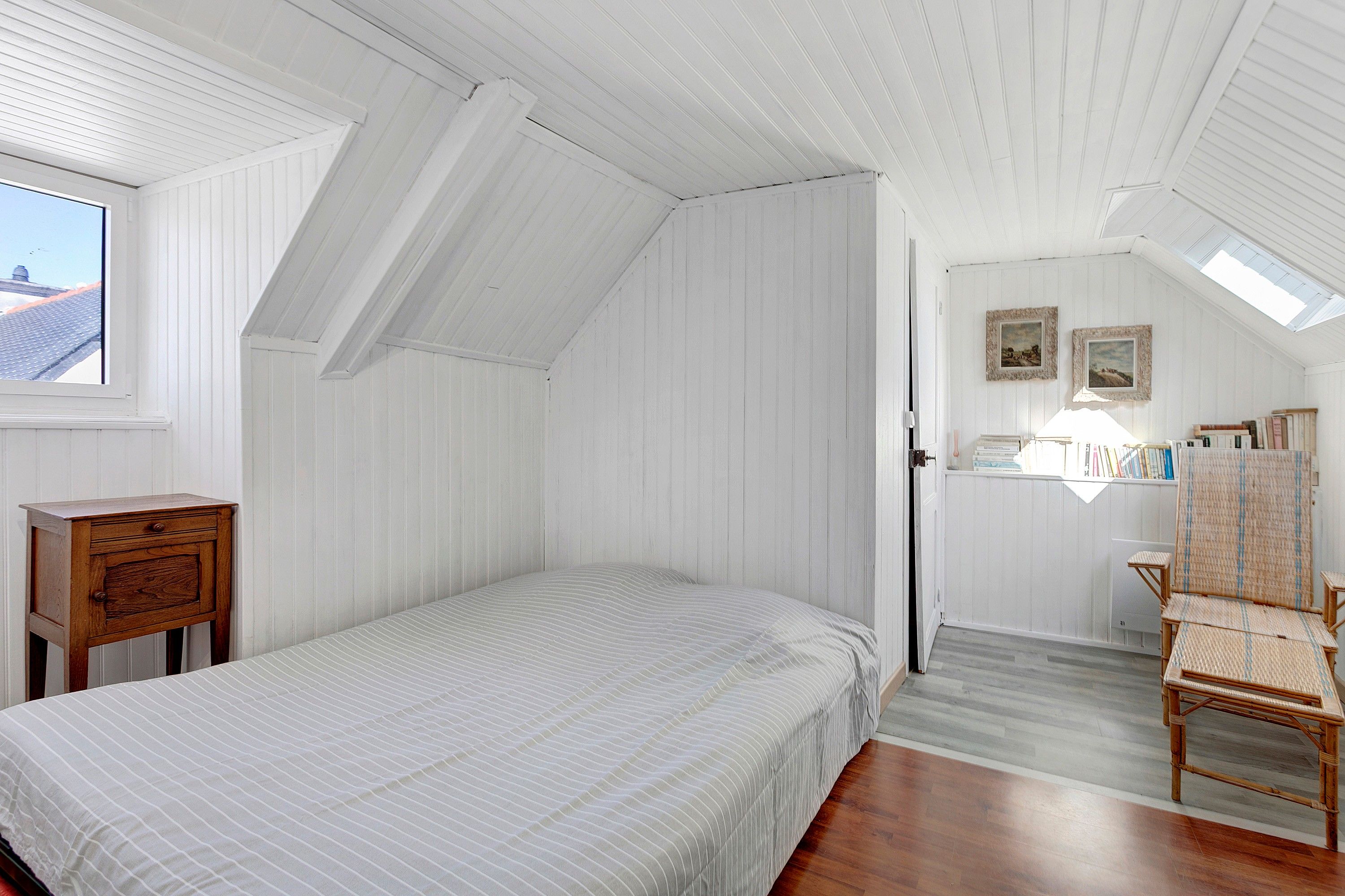 Une chambre avec un lit simple, une table de chevet en bois, une chaise et une lucarne.