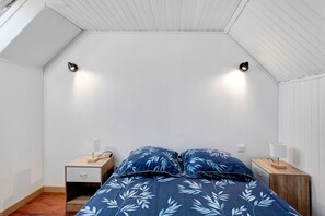 A bedroom with a sloped ceiling, a bed with a blue floral bedspread, two bedside tables with lamps, and a nightstand with a drawer.