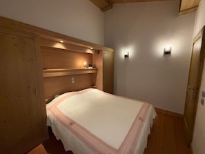 A bedroom with a bed, wooden wardrobe, and wall-mounted lights. - Apartment 8 guests, pets welcome, mountain view (Villard-sur-Doron)