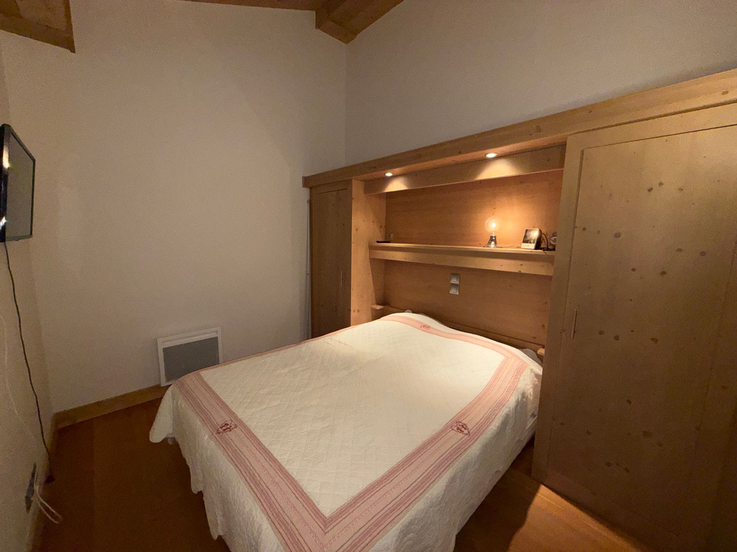 Un dormitorio con cama, mesita de noche, estante con lámpara y armario de madera.