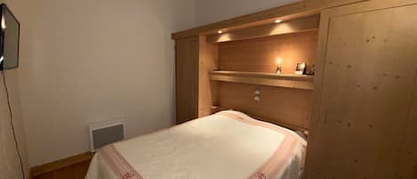 Un dormitorio con cama, mesita de noche, estante con lámpara y armario de madera.
