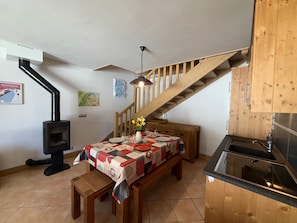 A cozy room with a wooden staircase, a dining table with a quilt, a wood-burning stove, and a kitchen area. - Apartment 8 guests, pets welcome, mountain view (Villard-sur-Doron)