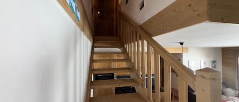 Una escalera de madera con barandilla que lleva a un dormitorio con cama y colcha.