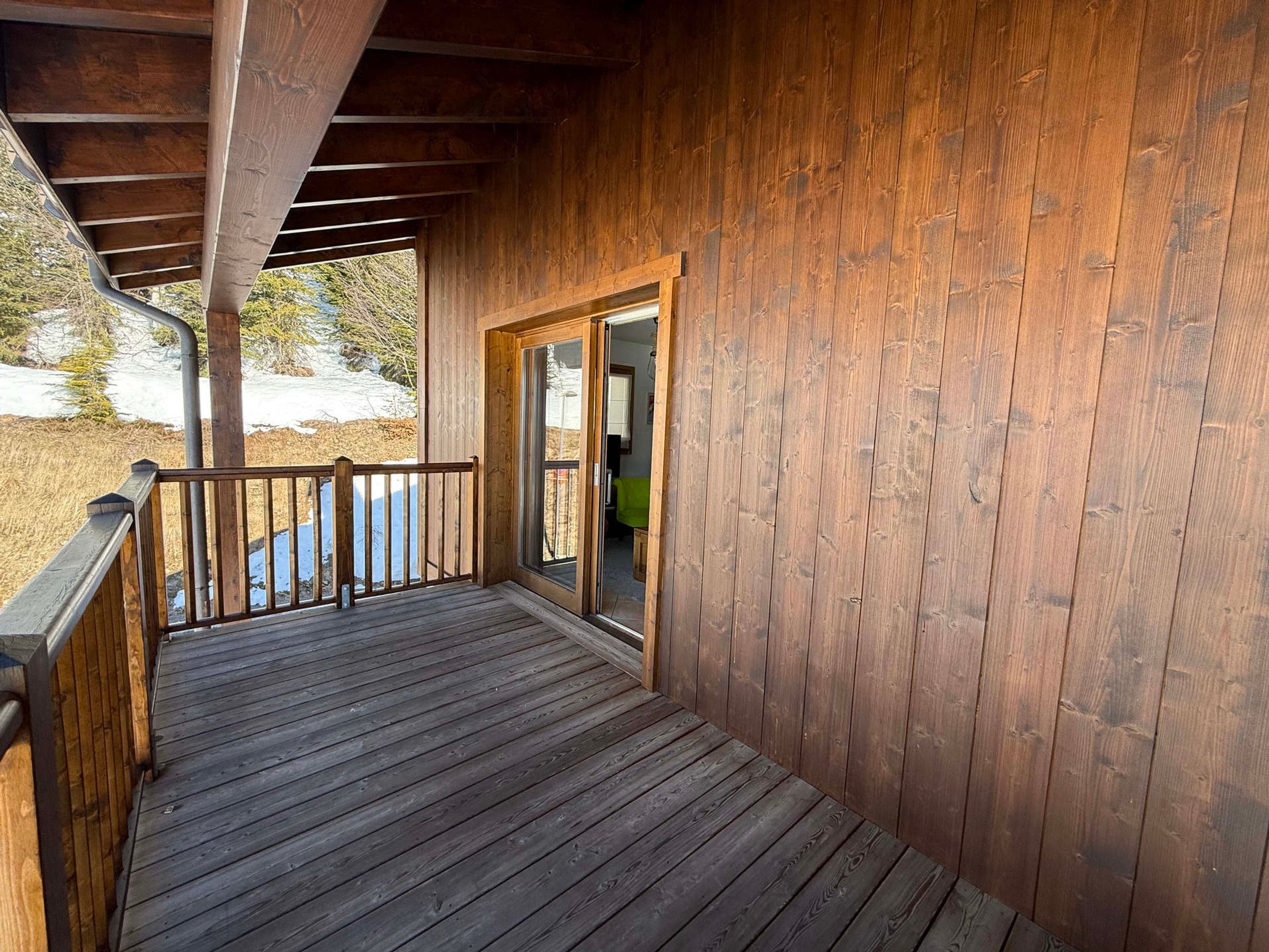 Une terrasse en bois avec une porte vitrée donnant sur un espace intérieur.