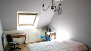 Ein Schlafzimmer mit Bett, Schreibtisch, Stuhl, Heizkörper und Fenster.