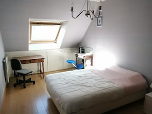 Ein Schlafzimmer mit Bett, Schreibtisch, Stuhl, Heizkörper und Fenster.