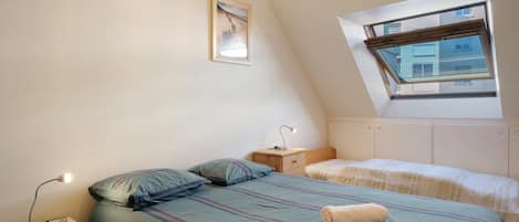 A bedroom with a bed, a bedside table, a lamp, a window, and a wall-mounted picture.