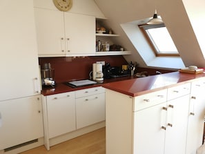 Eine Küche mit weißen Schränken, einer roten Arbeitsplatte, einer Kaffeemaschine und einem Oberlicht.