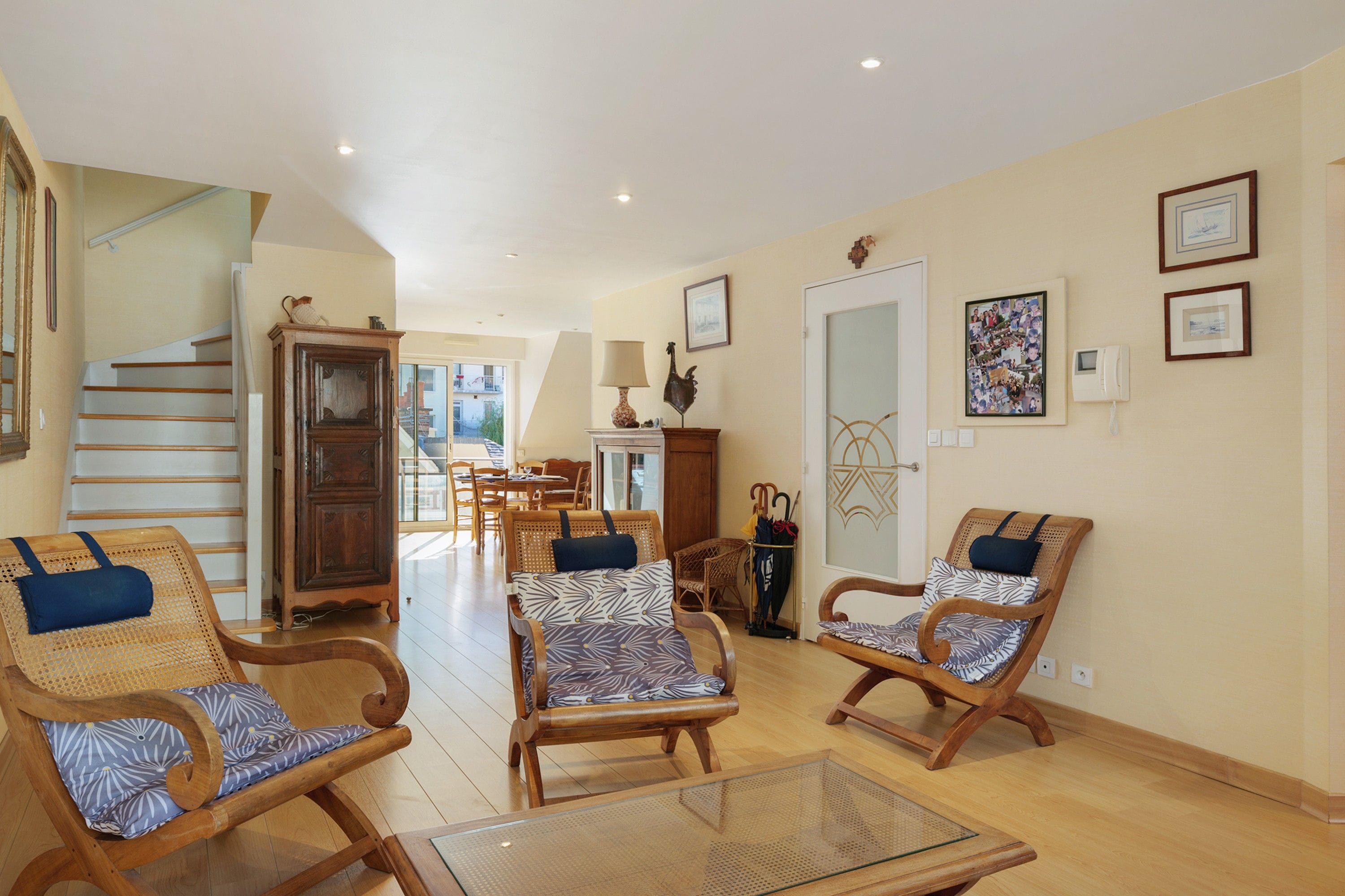 A spacious living room with a wooden staircase, a dining area, and a hallway leading to a door.
