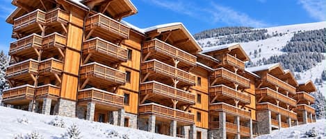 A multi-story wooden lodge with balconies, set against a snowy mountain backdrop.