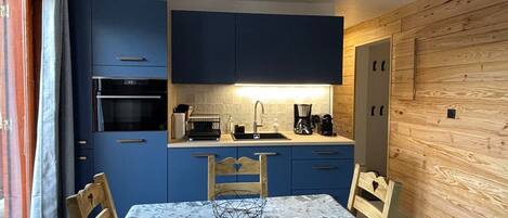 A compact kitchen with blue cabinets, a wooden dining table, and chairs.