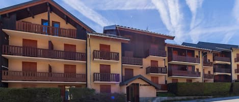 A row of multi-story buildings with balconies, a small entrance building, and a clear sky.
