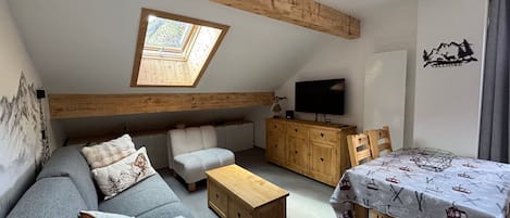 A cozy loft-style living space with a sloped ceiling, a built-in sofa, a wooden coffee table, and a dining table with a ski-themed tablecloth.