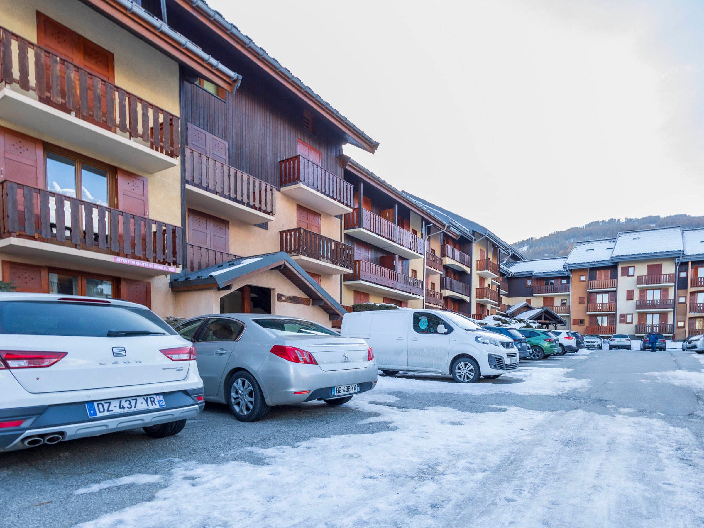 Una hilera de edificios de varios pisos con balcones, coches aparcados y suelo cubierto de nieve.