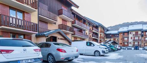 Una hilera de edificios de varios pisos con balcones, coches aparcados y suelo cubierto de nieve.