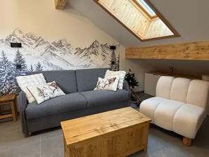 A living room with a grey sofa, a wooden coffee table, a white armchair, and a mountain mural on the wall. - Comfortable apartment, 6 guests (Valloire)