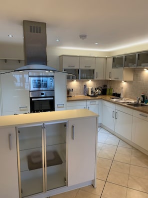 A modern kitchen with white cabinets, a stainless steel range hood, and a built-in oven.