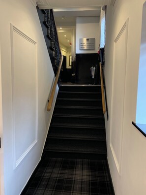 A staircase with a black carpet leading to a landing with a sign indicating apartment numbers. - The Residences Serviced Apartments (Aberdeen)