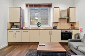 A compact kitchen with a microwave, stove, and sink, a small potted plant, and a sofa in the living area. - The Residences Serviced Apartments (Aberdeen)