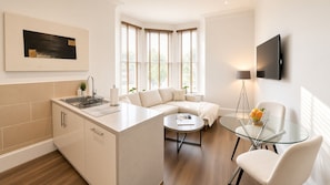 Una cocina moderna con una isla integrada, una zona de comedor con mesa de vidrio y un espacio de sala con sofá y televisor.